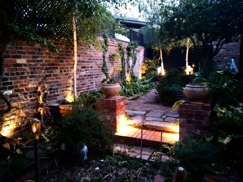 Path and garden lights along a brick wall at night