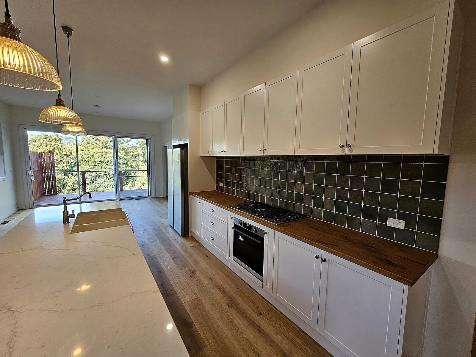 Three glass pendant lights and ceiling downlights over a kitchen bench